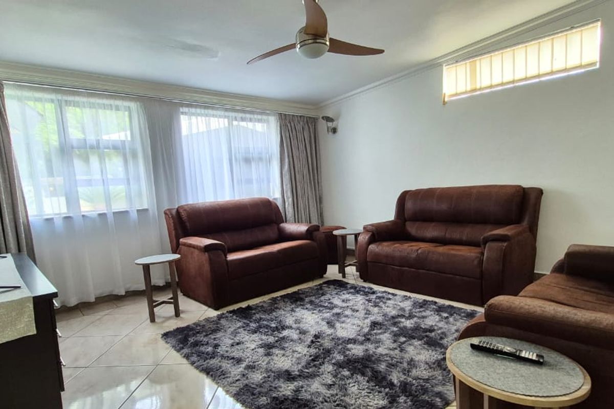 A comfortable living room featuring tiled flooring, a ceiling fan, and large windows with curtains, providing a bright and functional space.