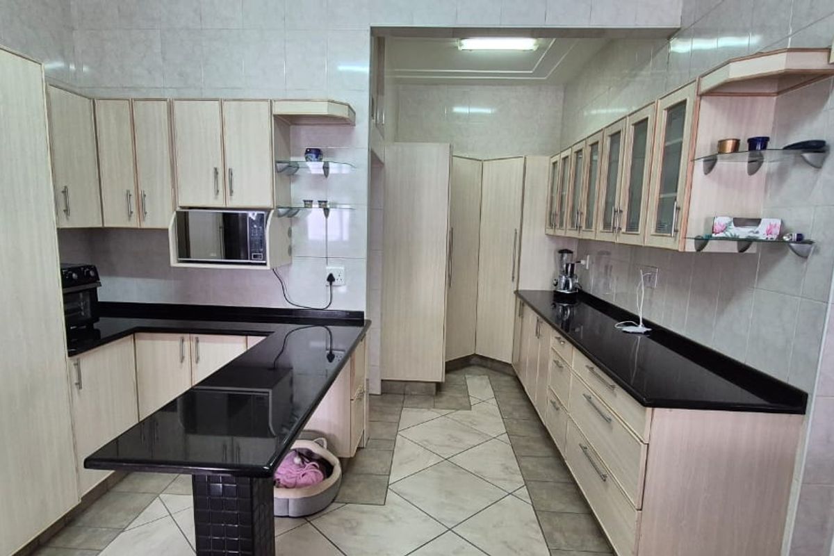 A functional kitchen featuring light wood-finish cabinetry, contrasting black granite countertops, tiled flooring, and integrated storage solutions.
