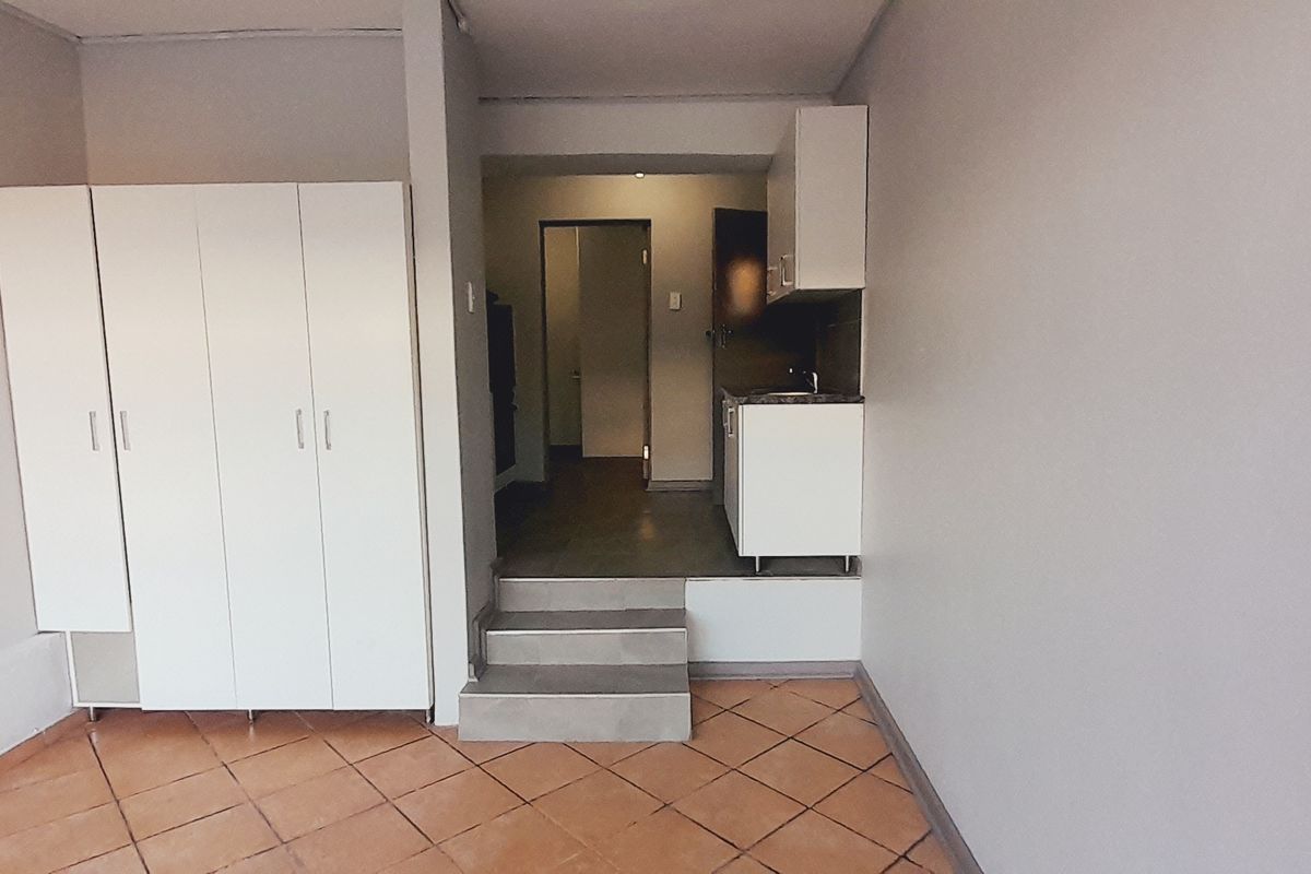 An open-plan living area featuring built-in cupboards, tiled flooring, and a raised kitchen section with cabinetry and a sink.