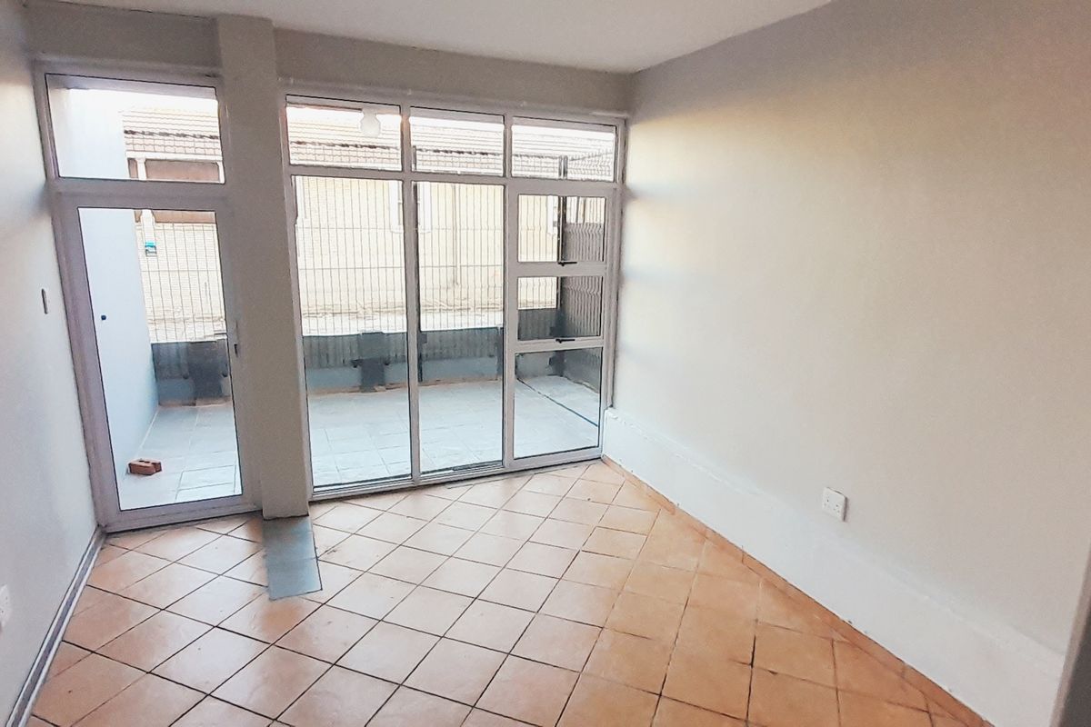An empty living room featuring tiled flooring and large aluminium sliding doors providing access to an outdoor area.