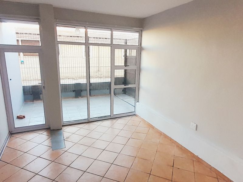 An empty living room featuring tiled flooring and large aluminium sliding doors providing access to an outdoor area.