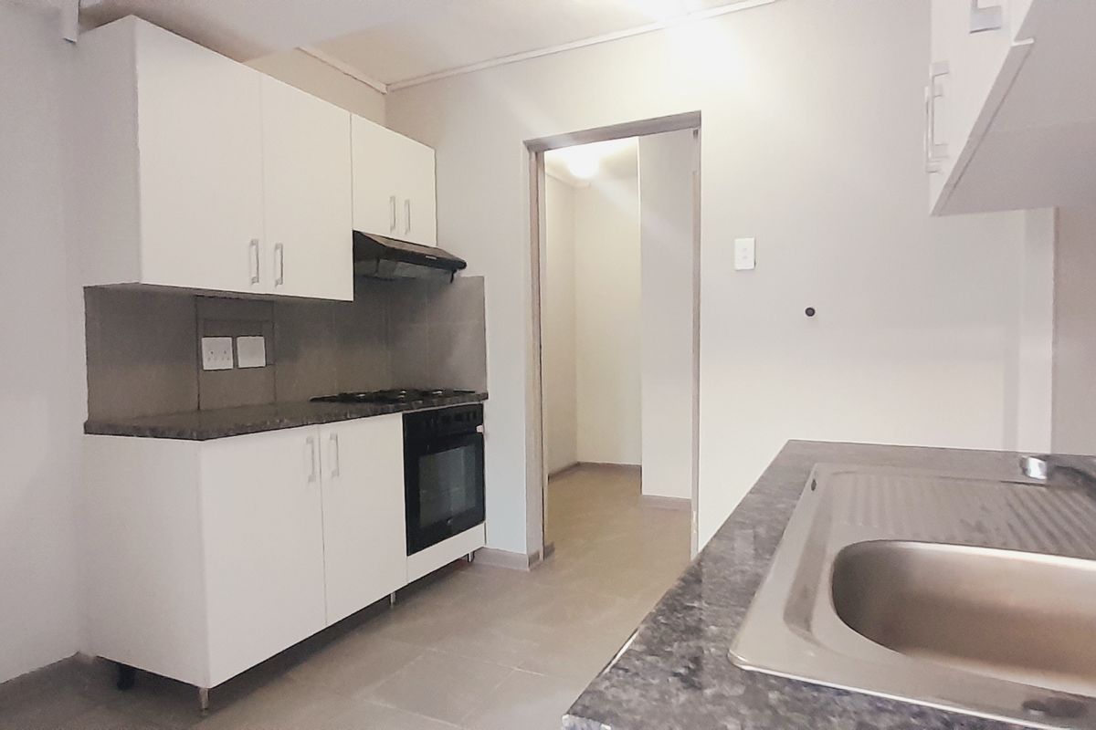 A functional, empty kitchen featuring white cabinetry, dark laminate countertops, a stainless steel sink, and built-in oven with gas hob and extractor fan.