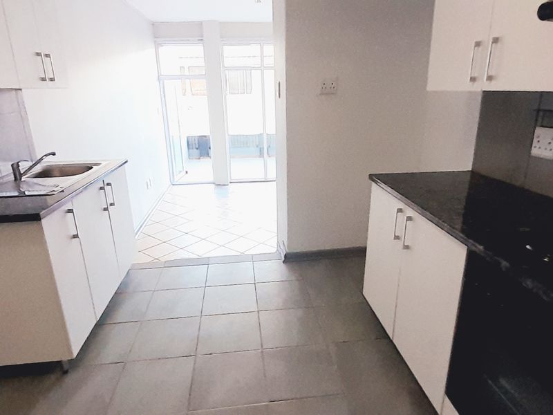 A functional galley-style kitchen featuring white cabinetry, dark countertops, built-in oven and hob, and tiled flooring, leading to an adjacent sunroom area.