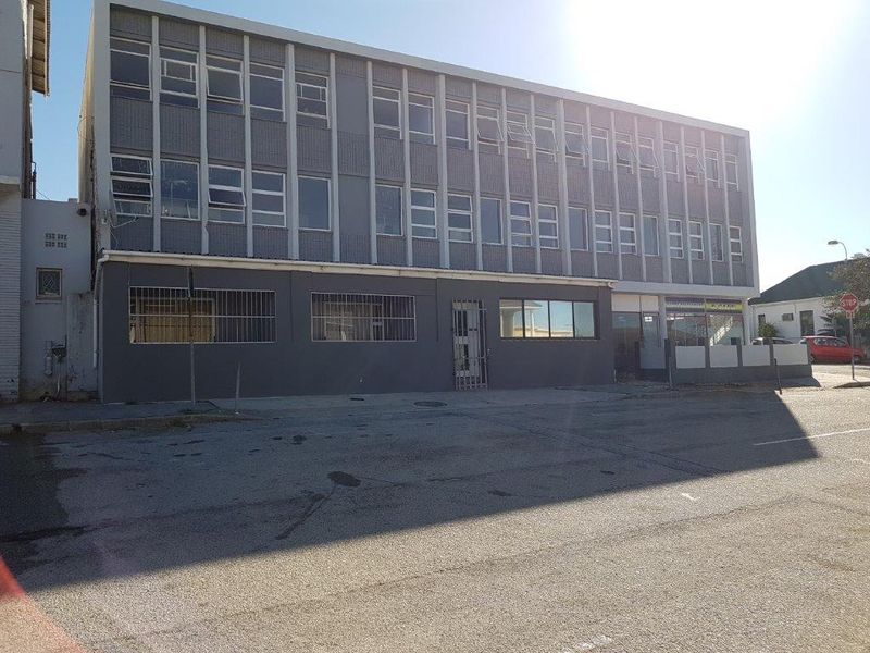 Front exterior view of a multi-story apartment building featuring a grey facade, aluminium window frames, and a paved street-level forecourt.