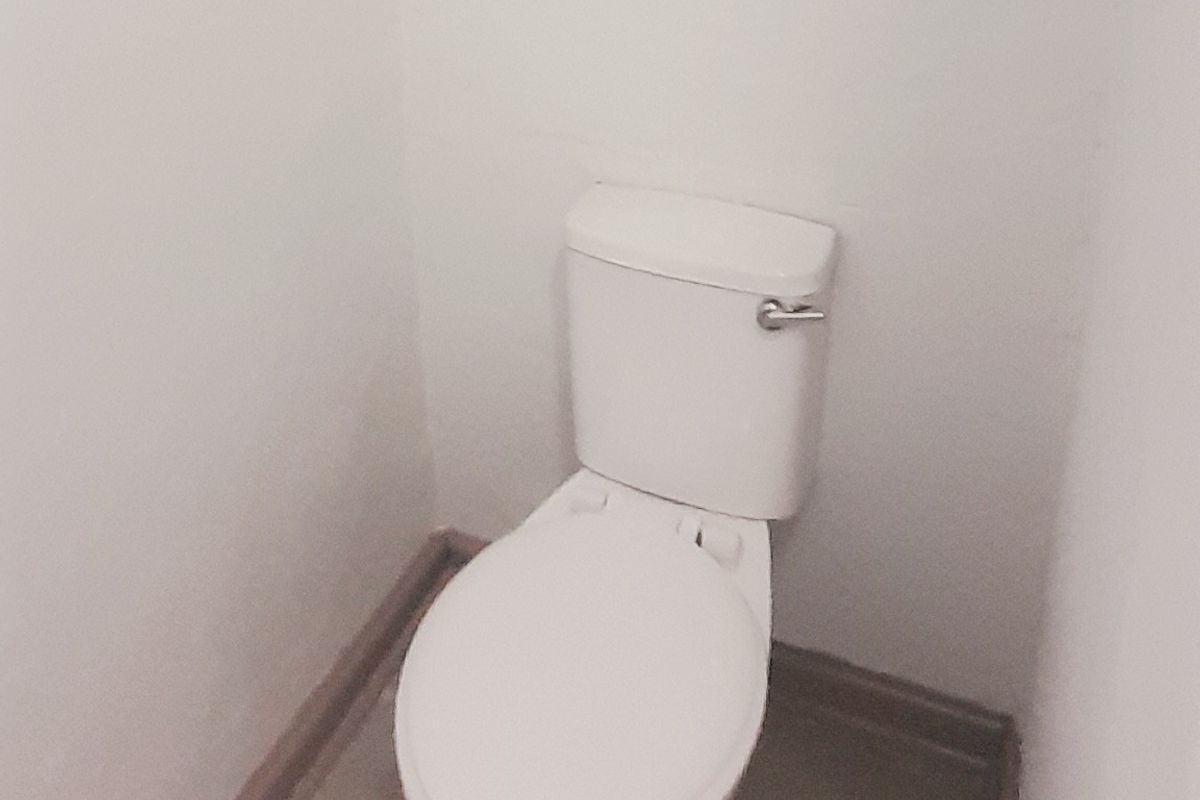 A simple, functional bathroom featuring a standard toilet, tiled flooring, and a window for natural light.