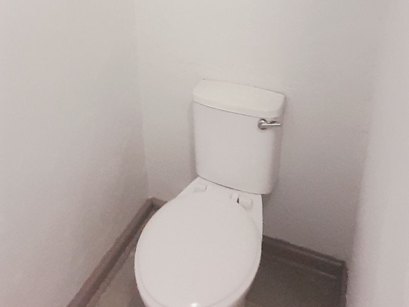 A simple, functional bathroom featuring a standard toilet, tiled flooring, and a window for natural light.