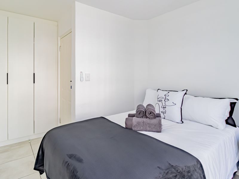 A clean and well-maintained bedroom featuring neutral white walls, tiled flooring, and ample built-in cupboard storage.
