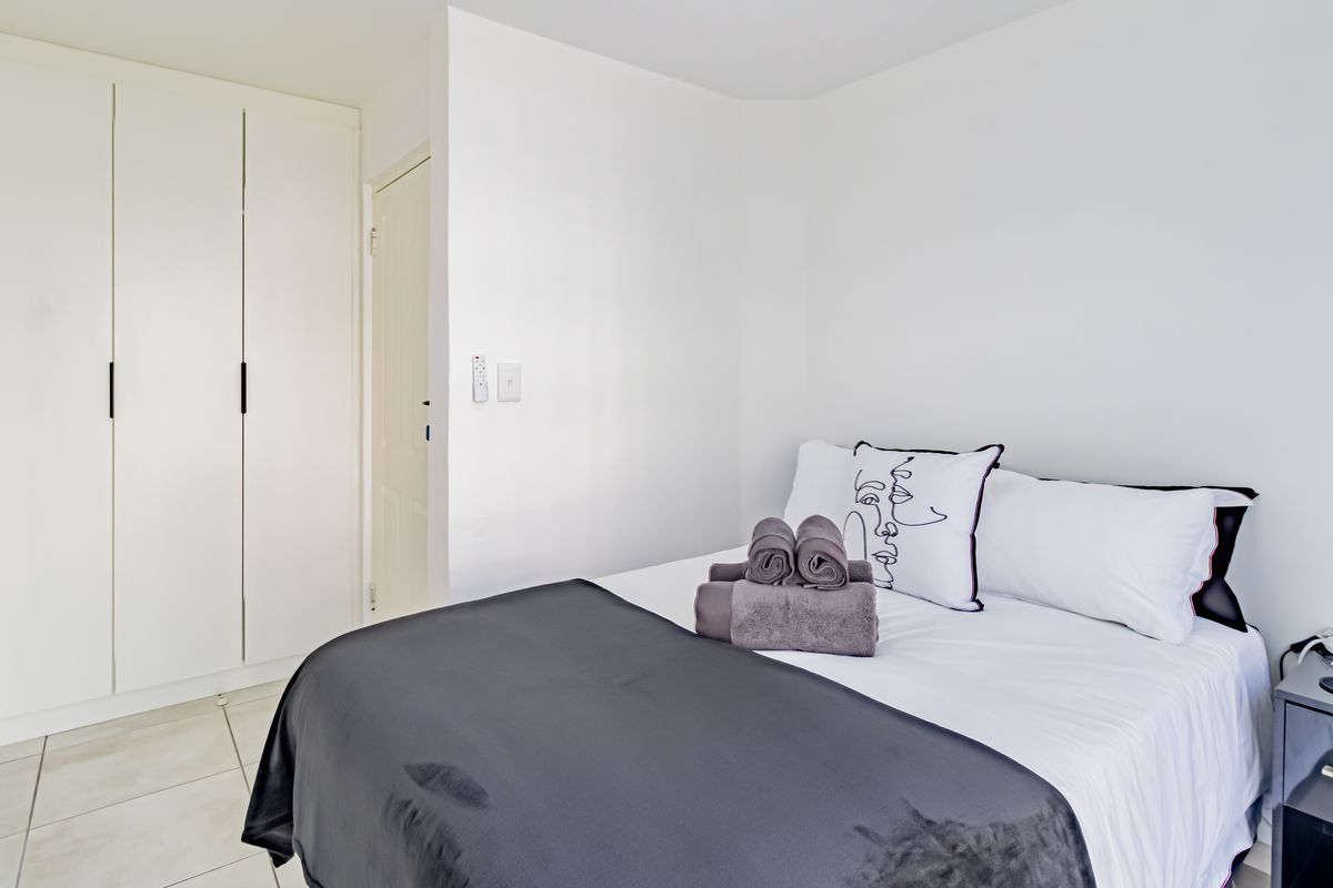 A clean and well-maintained bedroom featuring neutral white walls, tiled flooring, and ample built-in cupboard storage.