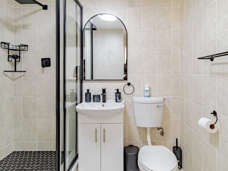 Modern bathroom featuring a walk-in shower with black-framed glass, a vanity basin, and a toilet, finished with neutral wall tiles and dark floor tiles.