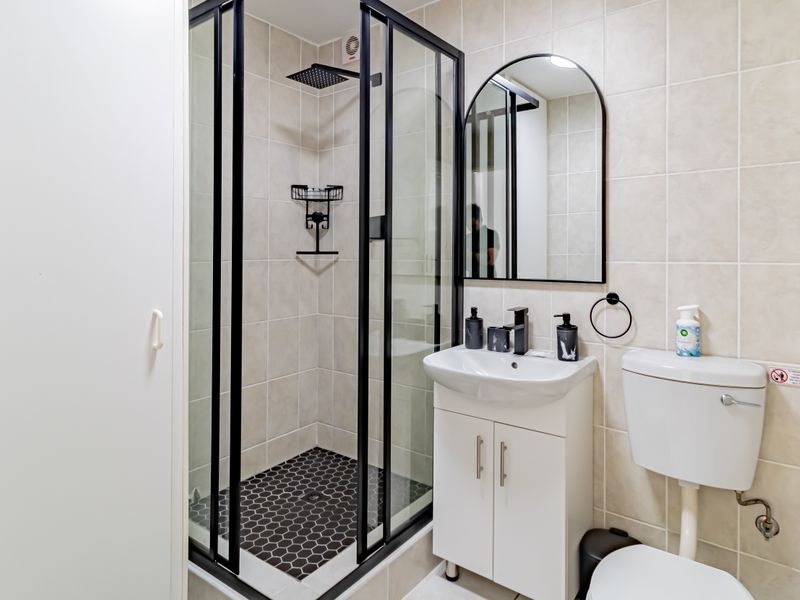 Modern bathroom featuring a glass-enclosed shower with black frame, vanity unit with basin, and neutral wall tiling.