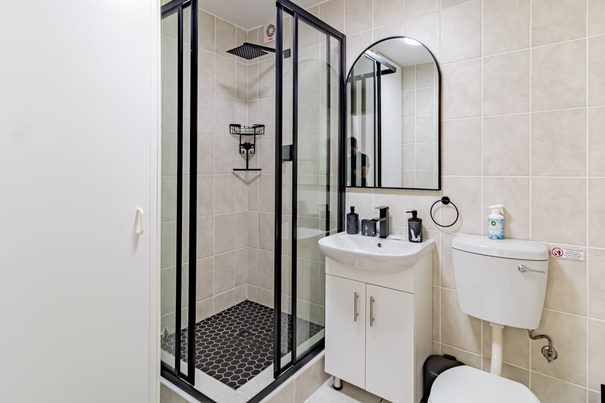 Modern bathroom featuring a glass-enclosed shower with black frame, vanity unit with basin, and neutral wall tiling.