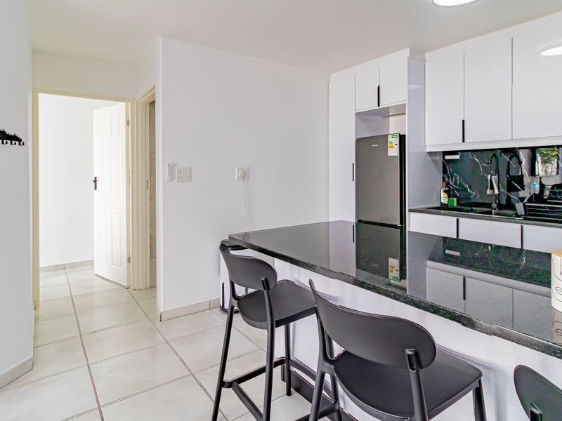 Modern kitchen featuring sleek white cabinetry, contrasting black granite countertops, and a stylish marble-look backsplash with tiled flooring.