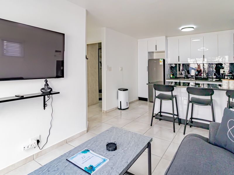 Modern open-plan living area featuring a sleek kitchen with high-gloss cabinetry, granite countertops, and tiled flooring throughout, creating a seamless and functional living space.