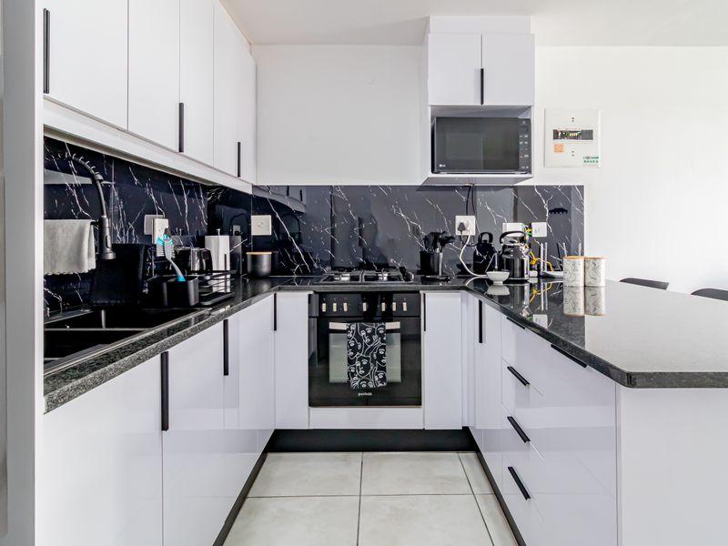 Modern U-shaped kitchen featuring white high-gloss cabinetry, black marble-look splashbacks, stone countertops, and integrated appliances including an oven and gas hob.