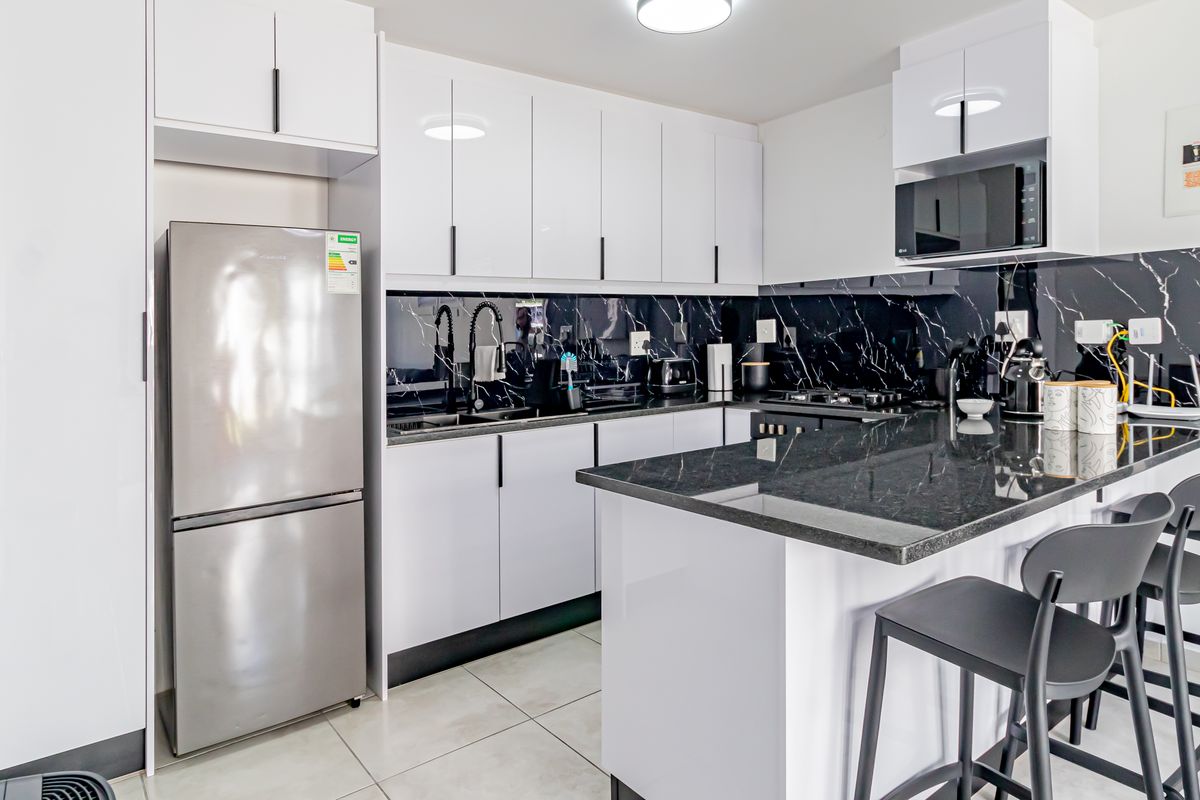 Modern kitchen featuring high-gloss white cabinetry, black marble-look splashback, granite-look countertops, a functional kitchen island, and integrated appliances.
