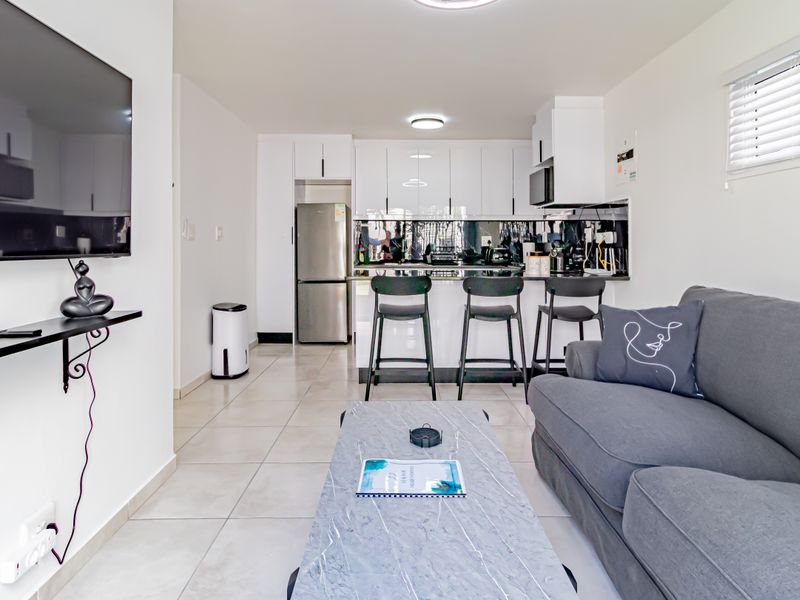 Modern open-plan living area featuring a sleek kitchen with white cabinetry, tiled floors, and a breakfast bar, seamlessly integrated with the lounge space.