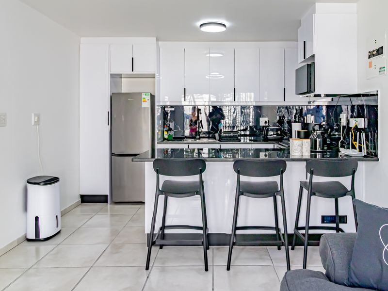 Modern open-plan kitchen featuring sleek white cabinetry, black stone countertops, and a stylish tiled backsplash, seamlessly integrated into the living space.