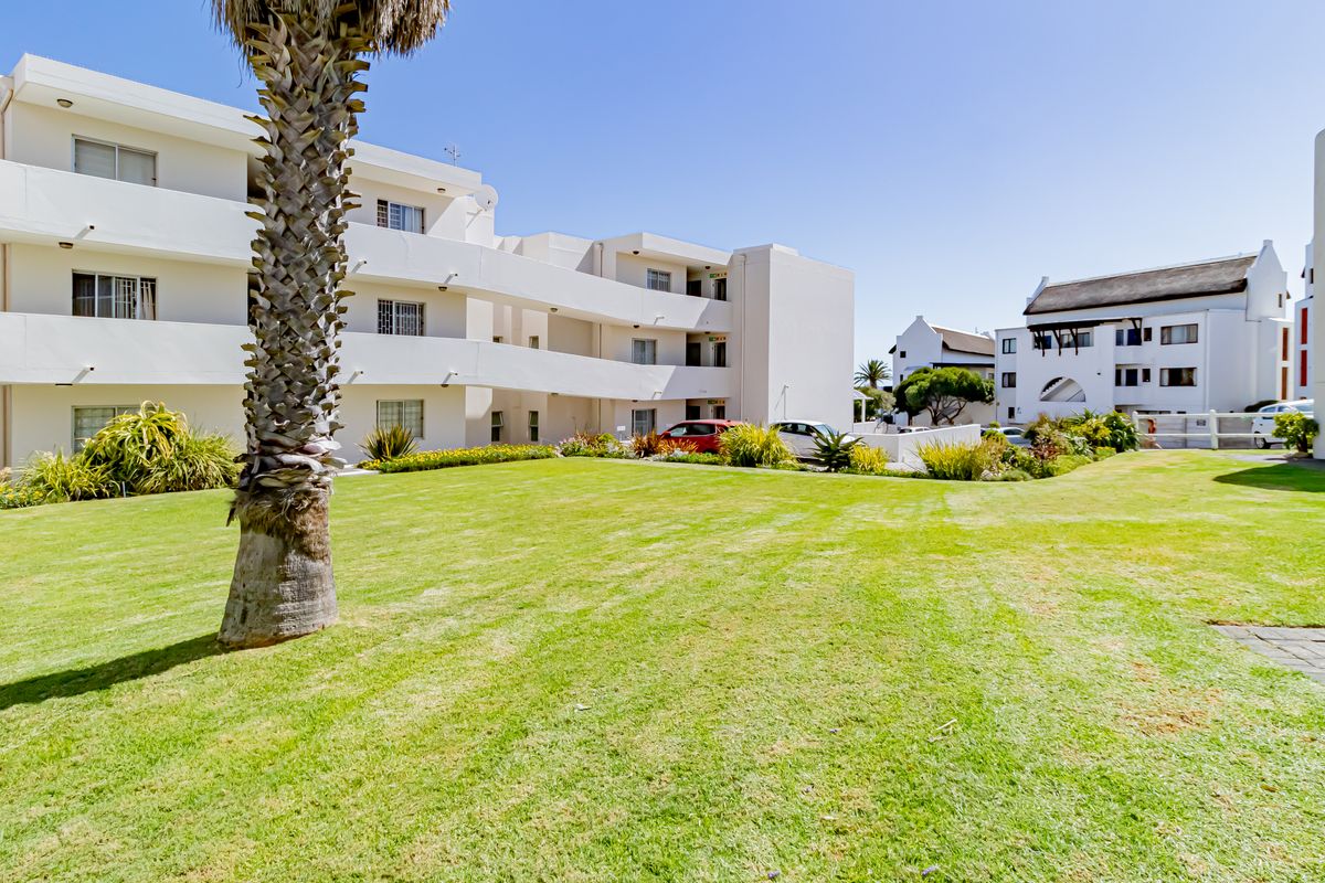 A well-maintained communal garden area featuring a manicured lawn, paved pathways, and views of the apartment building's exterior balconies.