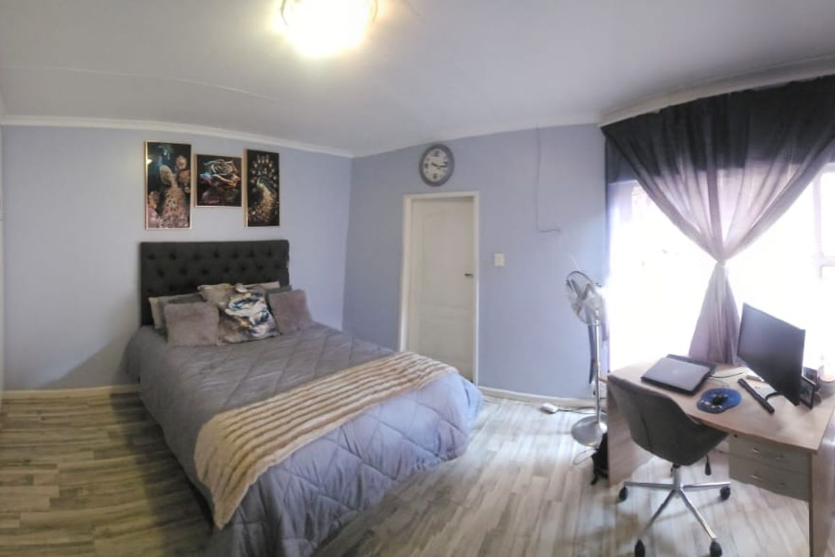 A bedroom featuring built-in cupboards, light-toned wood-look flooring, and a window with curtaining.