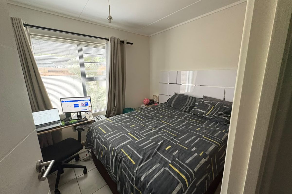 A functional bedroom featuring tiled flooring, window blinds, and a built-in headboard, offering a practical space for rest and work.