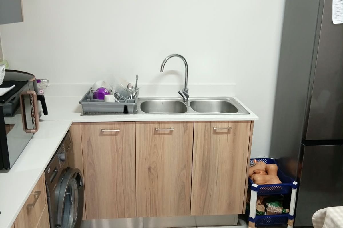 A functional kitchen area featuring light wood-finish cabinetry, a double bowl sink with mixer tap, tiled flooring, and integrated laundry and cooking appliances.