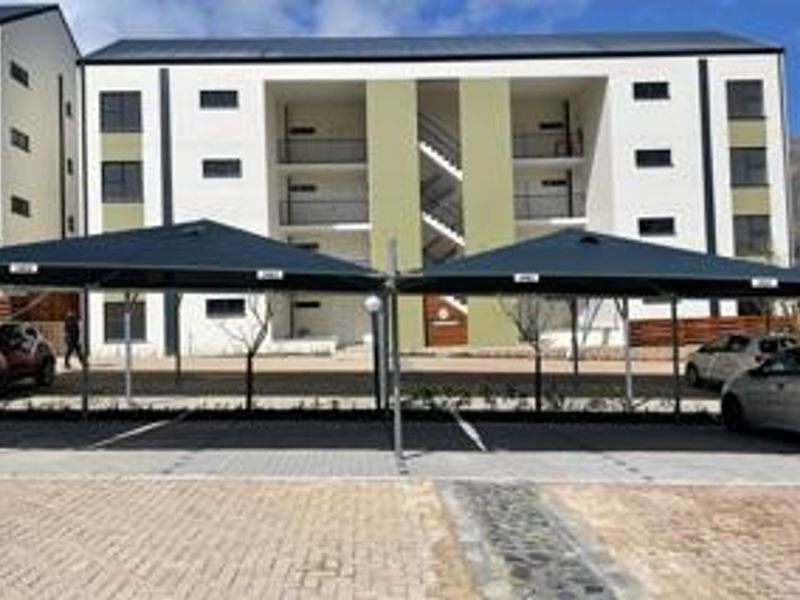 Front view of a modern multi-story apartment complex featuring dedicated shade cloth parking bays and paved driveway access.