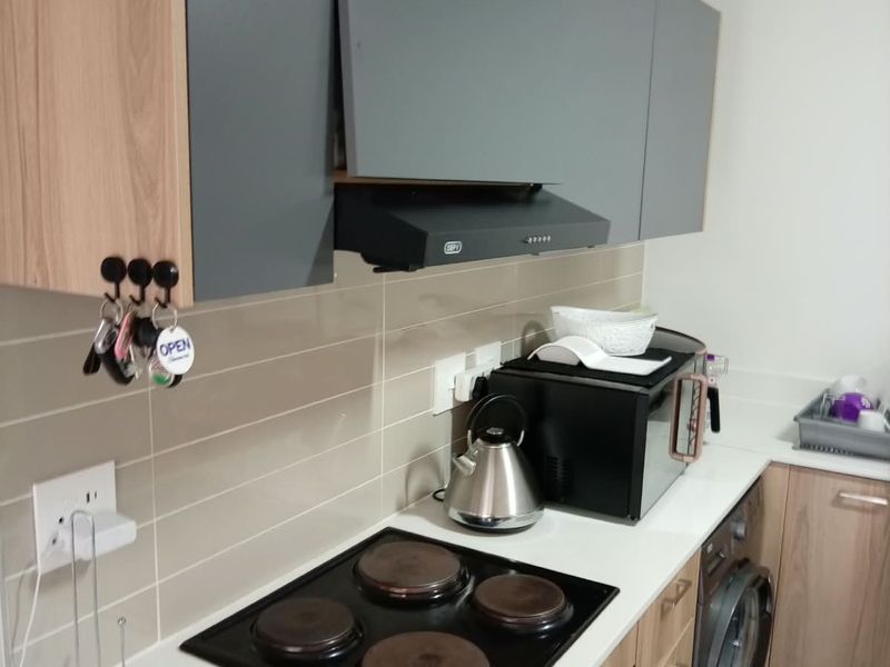 Compact kitchen featuring modern two-tone cabinetry, built-in electric hob and oven, extractor fan, and integrated laundry appliance with tiled backsplash.