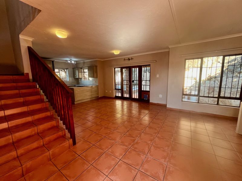 Spacious open-plan living area featuring tiled flooring, a wooden staircase, and direct access to the outdoor area through glass panel doors.