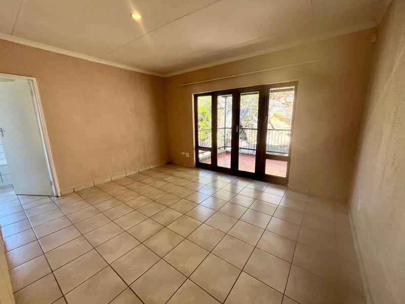 An empty living room featuring tiled flooring and large sliding glass doors that provide direct access to an outdoor balcony area.