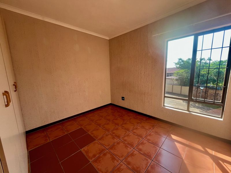 An empty bedroom featuring tiled flooring, built-in cupboards, and a window with security bars, offering a blank canvas for potential updates.
