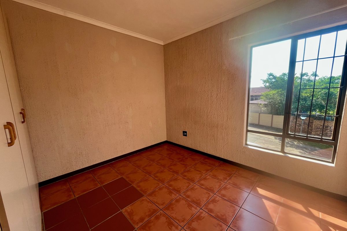 An empty bedroom featuring tiled flooring, built-in cupboards, and a window with security bars, offering a blank canvas for potential updates.