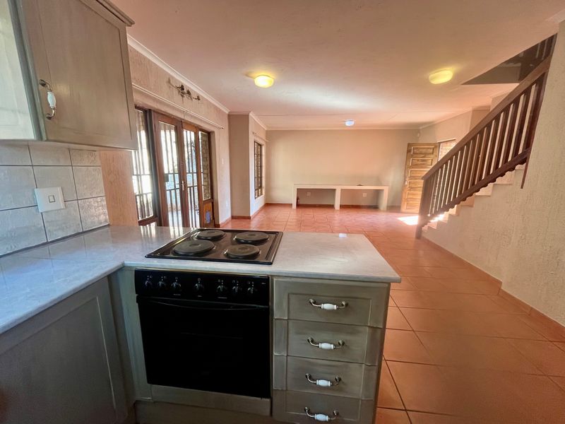 Open-plan kitchen and living area featuring tiled floors, built-in cabinetry with integrated oven and hob, and a staircase leading to the upper level.