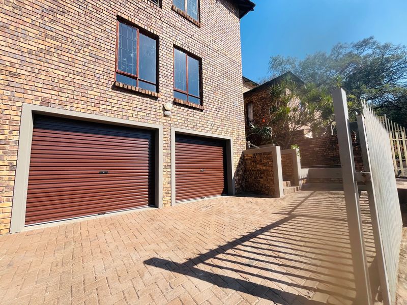 A well-maintained double garage with roller shutter doors, brick facade, and paved driveway, secured by metal fencing.