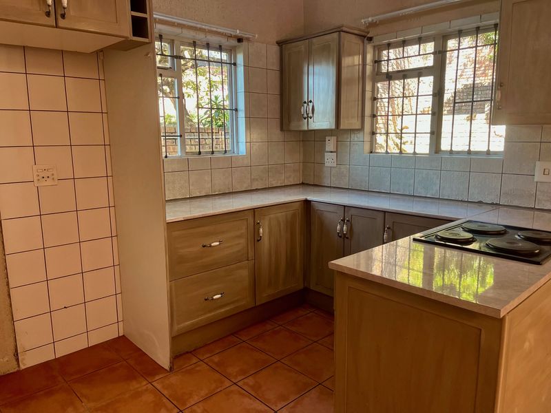 A functional kitchen featuring built-in cabinetry, laminate countertops, an electric hob, and tiled splashbacks, offering a practical layout ready for modernization.