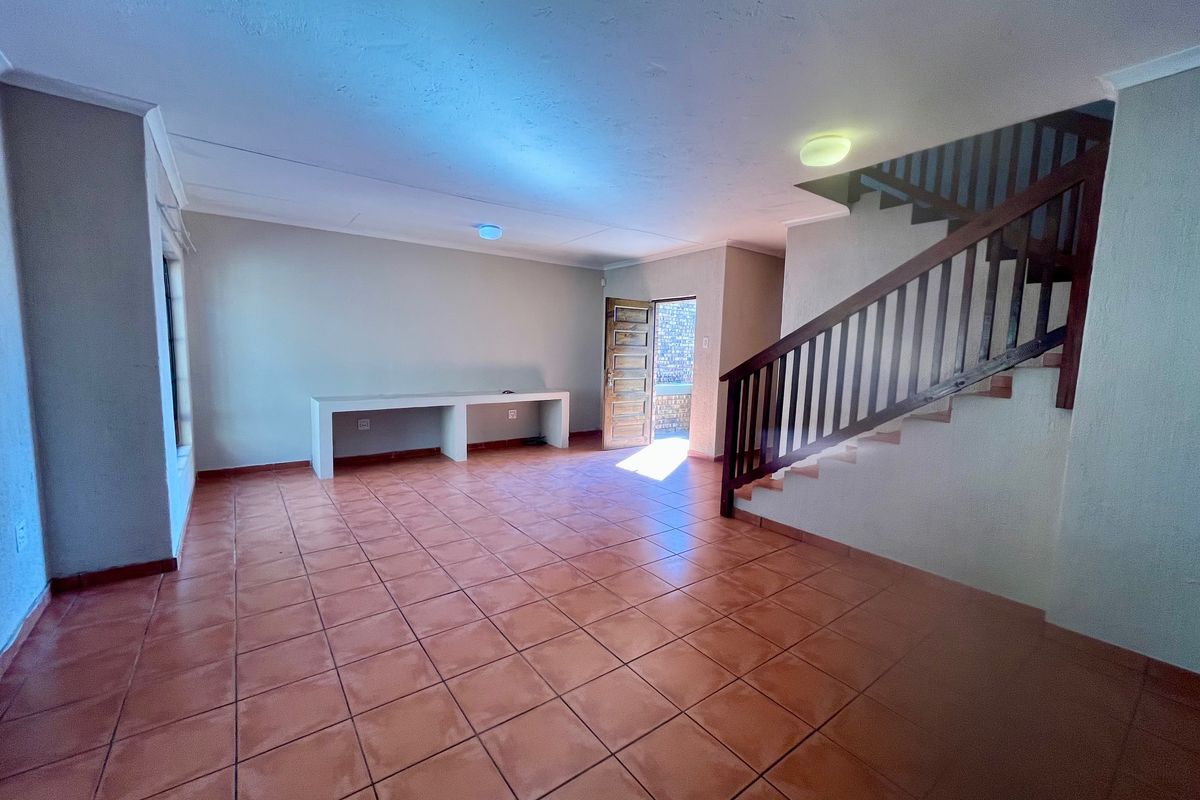 Spacious living area featuring terracotta tiled flooring, a built-in desk, and a wooden staircase leading to the upper level.