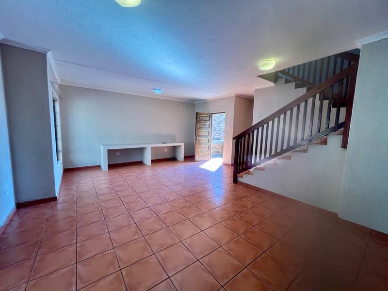 Spacious living area featuring terracotta tiled flooring, a built-in desk, and a wooden staircase leading to the upper level.
