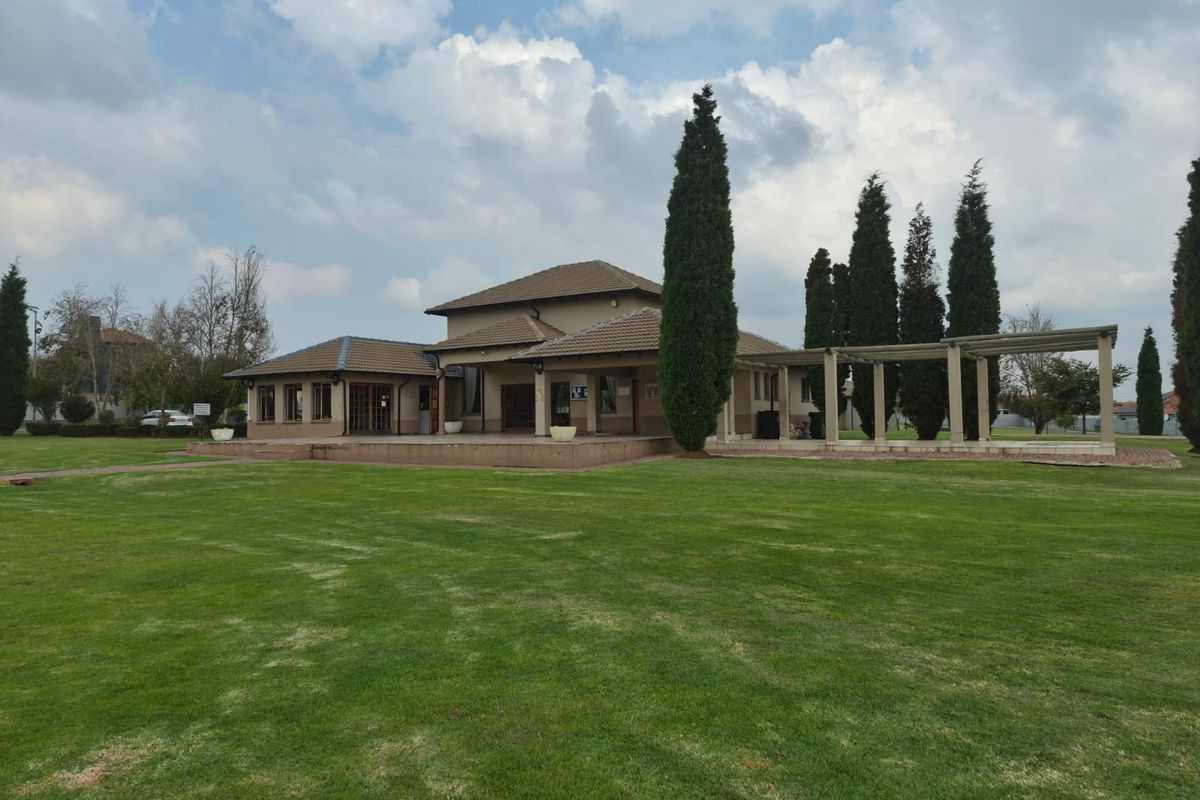 A view of the rear exterior of the townhouse featuring a paved patio area, a pergola, and a well-maintained lawn.