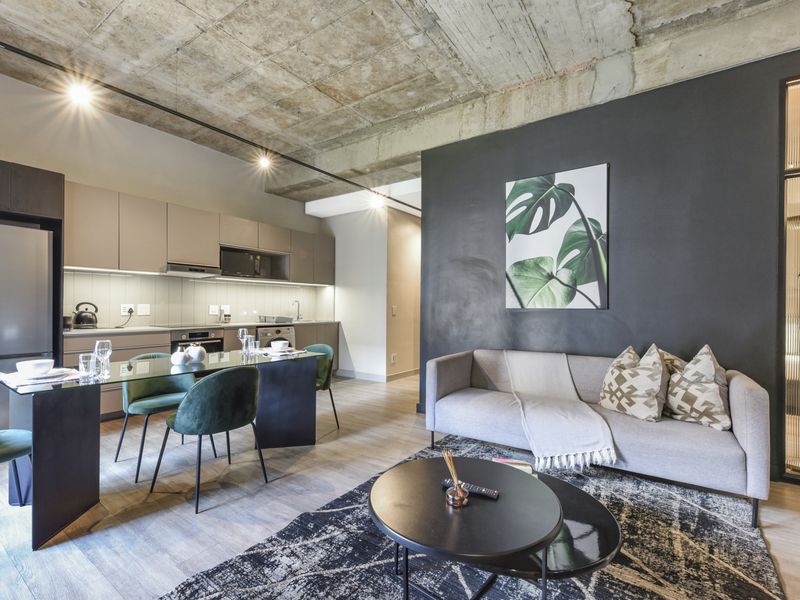 Modern open-plan apartment featuring an exposed concrete ceiling, sleek kitchen cabinetry with integrated appliances, and a stylish fluted glass room divider.