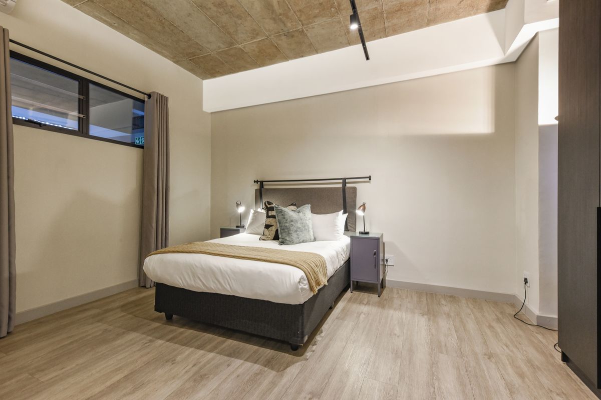 Modern bedroom featuring an exposed concrete ceiling, laminate flooring, and a built-in wardrobe, offering a contemporary industrial aesthetic.