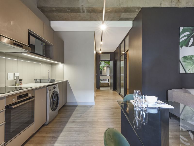 Modern open-plan kitchen featuring sleek cabinetry, integrated appliances, and high-quality finishes, seamlessly flowing into the living area under an exposed concrete ceiling.