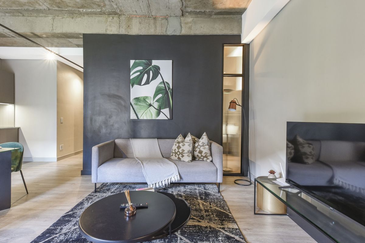 Modern living room featuring an exposed concrete ceiling, sleek dark accent wall, and a stylish fluted glass partition.