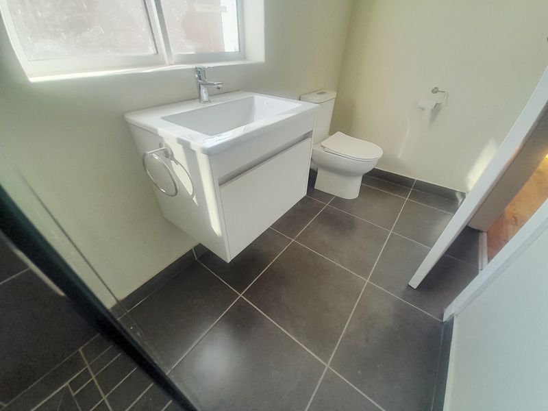 A clean, modern bathroom featuring a wall-mounted vanity with basin, toilet, and dark tiled flooring.