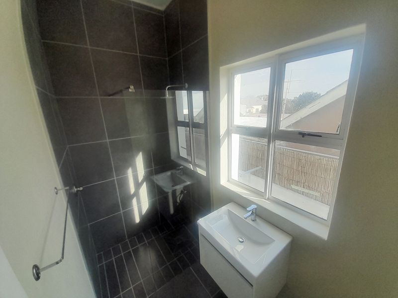 A modern bathroom featuring a tiled shower enclosure, a wall-mounted basin with a vanity cabinet, and a large window providing natural light.