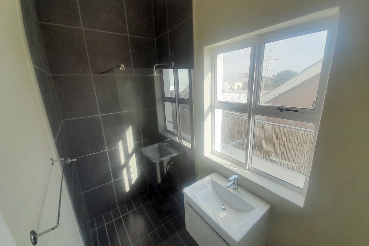 A modern bathroom featuring a tiled shower enclosure, a wall-mounted basin with a vanity cabinet, and a large window providing natural light.