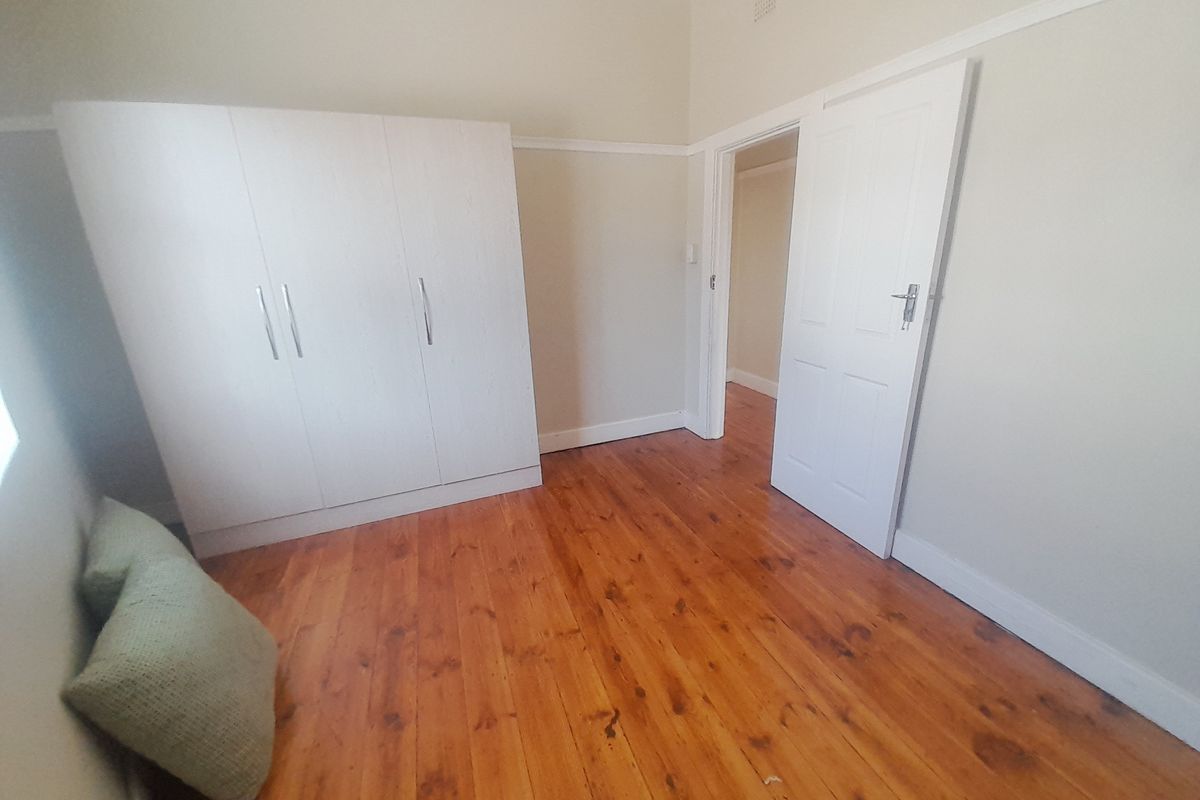 A bright bedroom featuring polished timber flooring, neutral wall tones, and a built-in wardrobe with white cabinetry.