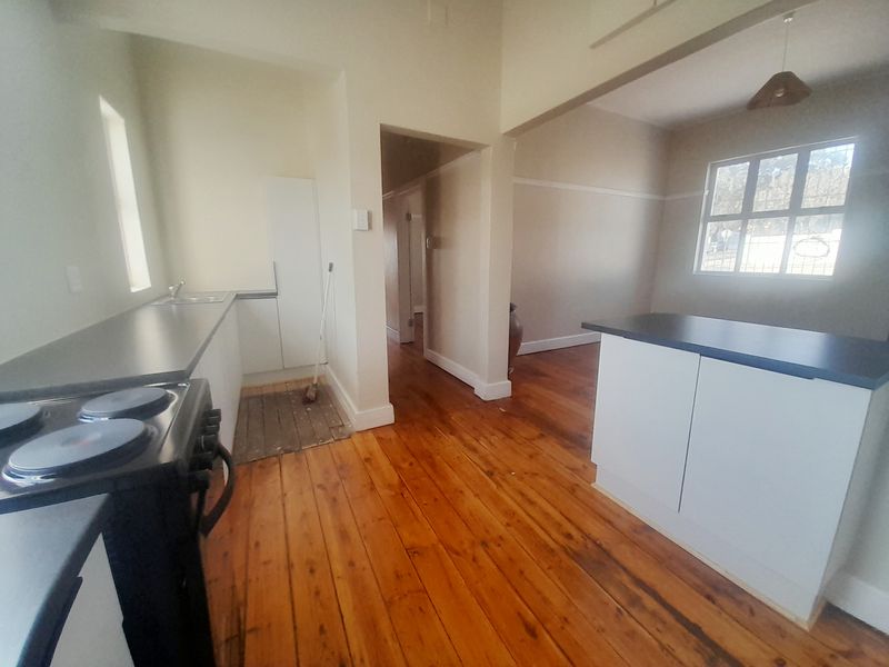 Open plan kitchen and living area featuring original hardwood flooring, white cabinetry, and an electric stove, offering a blank canvas for modern updates.