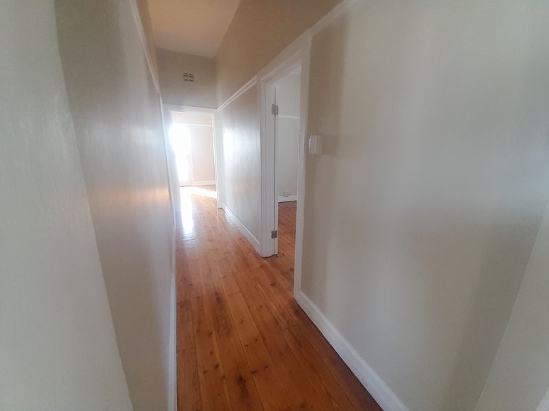 A bright, empty hallway featuring polished timber flooring, classic picture rails, and white-painted walls connecting multiple rooms.