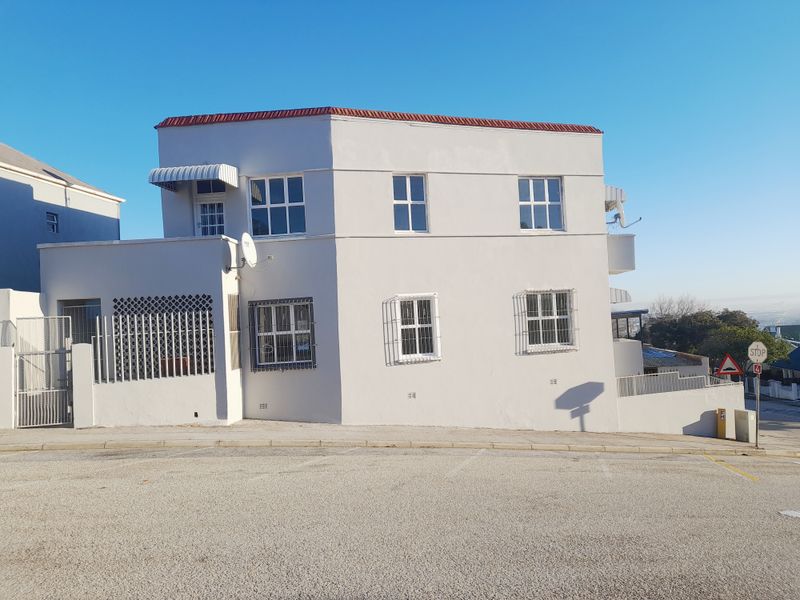 Street-facing view of a two-story apartment building featuring white exterior walls, security bars on windows, and a tiled roof.