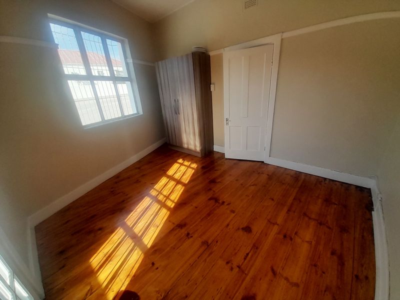 A bright, empty bedroom featuring polished timber flooring, a picture rail, and a window fitted with security bars.