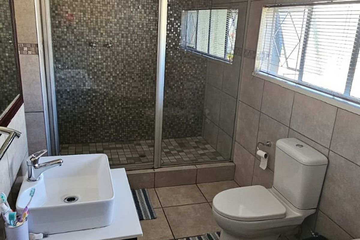 A functional bathroom featuring a glass-enclosed shower with mosaic tiling, a modern vessel sink, a toilet, and a bathtub.